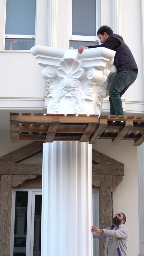 Un operaio cammina su una piattaforma di carrello elevatore accanto a un grande capitello decorativo.