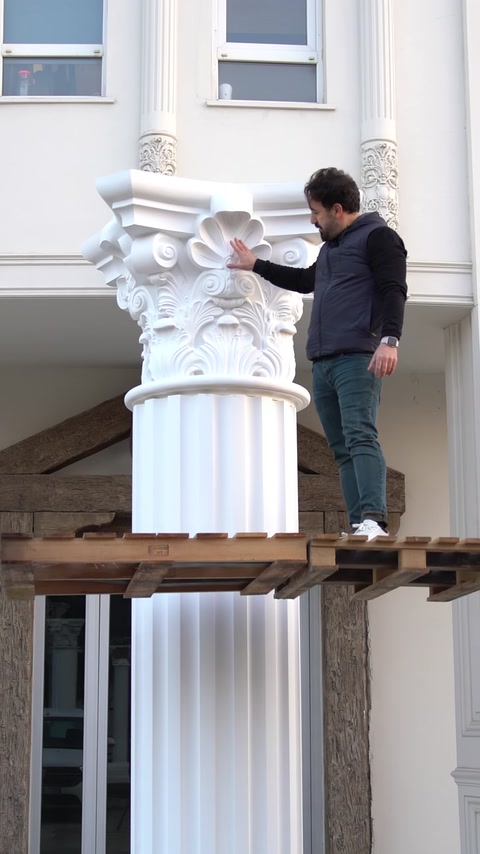 Un operaio si trova accanto a una colonna completamente assemblata con capitello installato.
