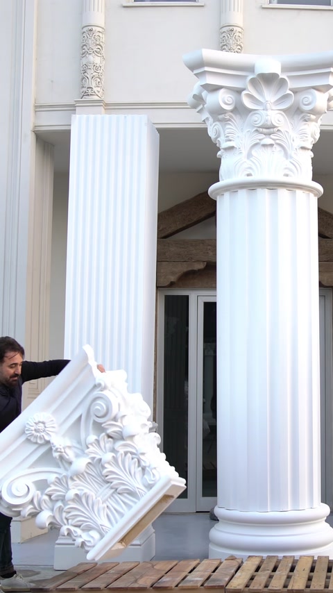 Un operaio abbassa un capitello decorativo su un fusto di colonna già installato.