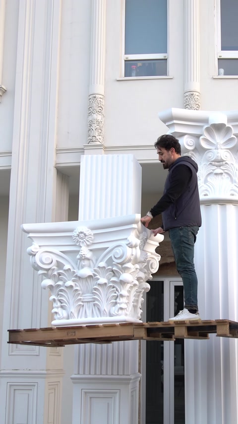 Un operaio su una piattaforma accanto a colonne installate lungo la facciata dell'edificio.