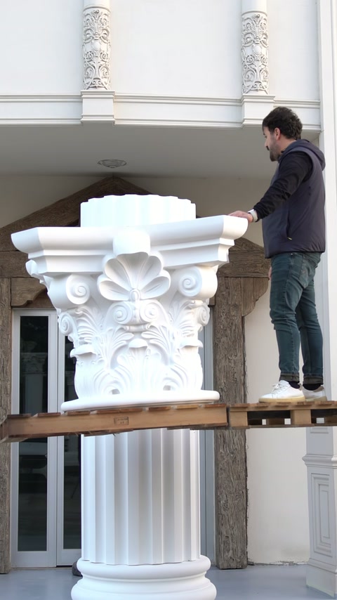 Un operaio guida un capitello ornato verso una colonna esterna verticale.