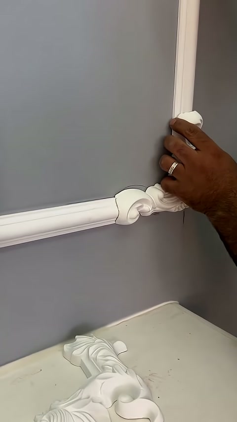 A carved detail piece is being fitted to the corner of the trim on the gray wall