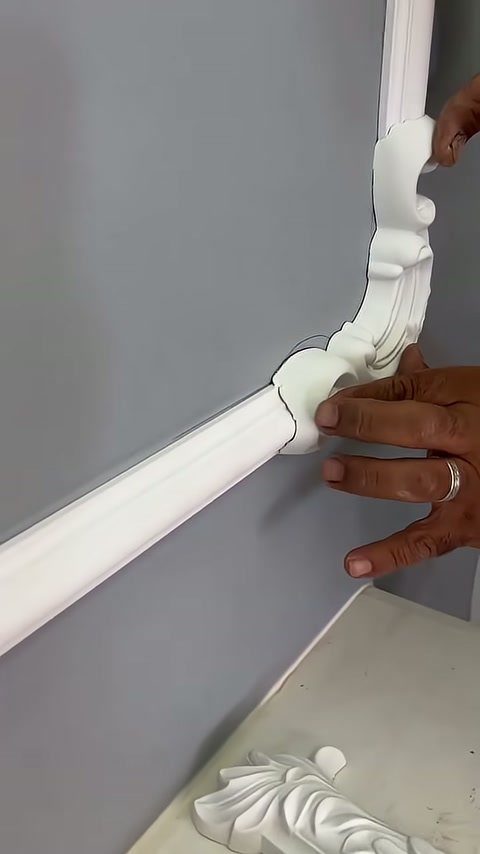 A curved corner element is being held in place on the gray wall from two directions