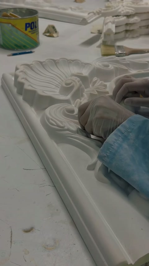 Mano guantata che leviga il lavoro intricato delle foglie su una cornice decorativa