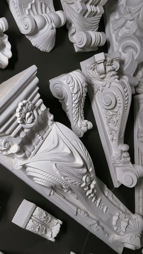 Embossed consoles and classical decorative pieces are displayed on a black exhibition surface.