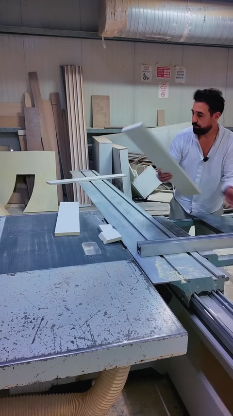 Un operaio solleva un pezzo di cornice tagliato sopra il piano della sega