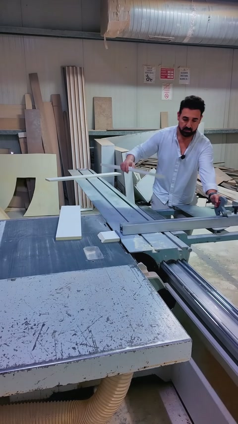 Worker guides white polyurethane cornice through the workshop sliding table saw.