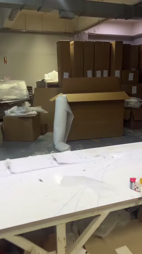 Üretim tezgâhı çevresinde koliler ve beyaz ambalaj malzemeleri görülüyor