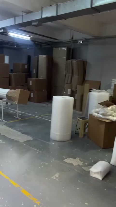 Atölyede uzun sütunlar, silindirik parçalar ve istiflenmiş koliler bulunuyor
