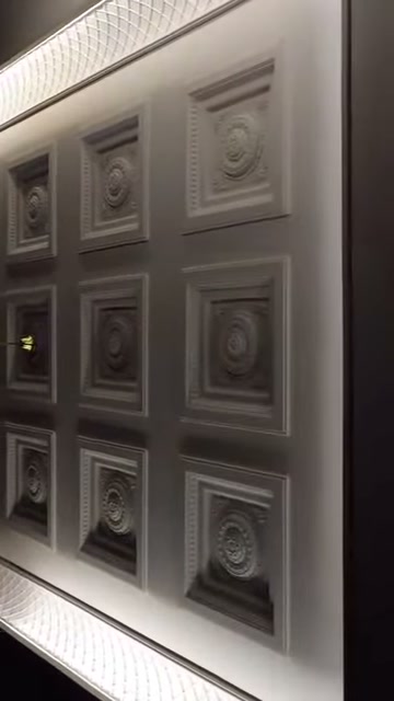 Sulla superficie bianca del soffitto si trovano moduli quadrati in rilievo di diverse dimensioni