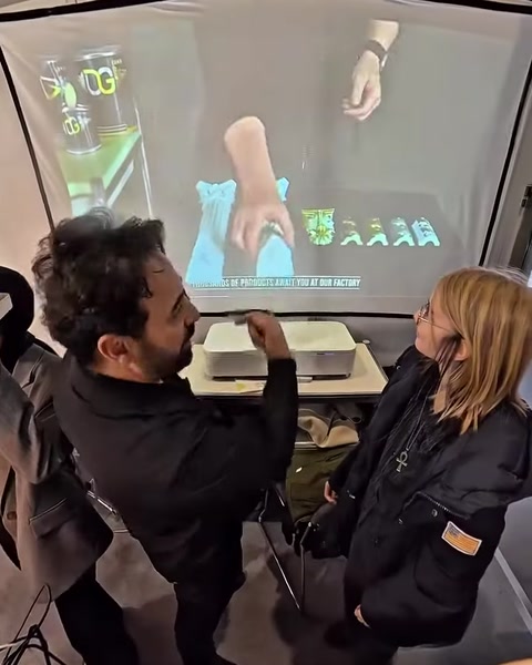 Görevli, projeksiyon önünde VR deneyiminin kullanımını ziyaretçiye açıklıyor