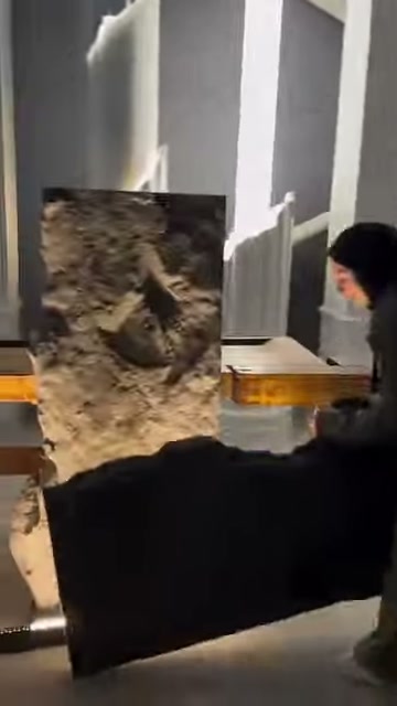 A dark-colored panel piece is held horizontally in front of a raised rock-look panel