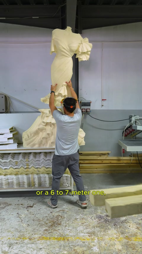 Un artigiano esamina in posizione verticale il grande rilievo a forma di abito da sposa nel laboratorio.