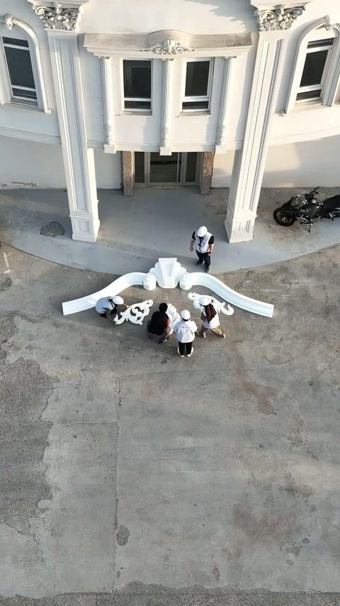 Gli operai iniziano a posare sezioni di cornice curva bianca sul cortile pavimentato.
