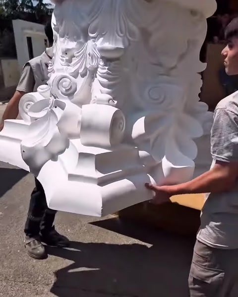 Due operatori trasportano il capitello decorato tenendolo da lati opposti