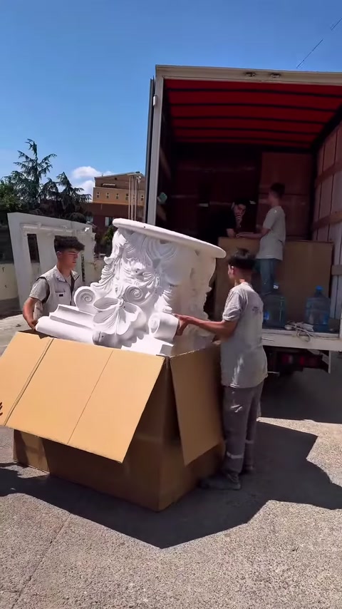 Gli operai sollevano insieme il capitello decorativo dalla scatola d'imballaggio