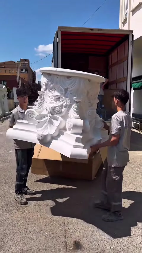 Due persone trasportano con cautela il grande capitello decorativo