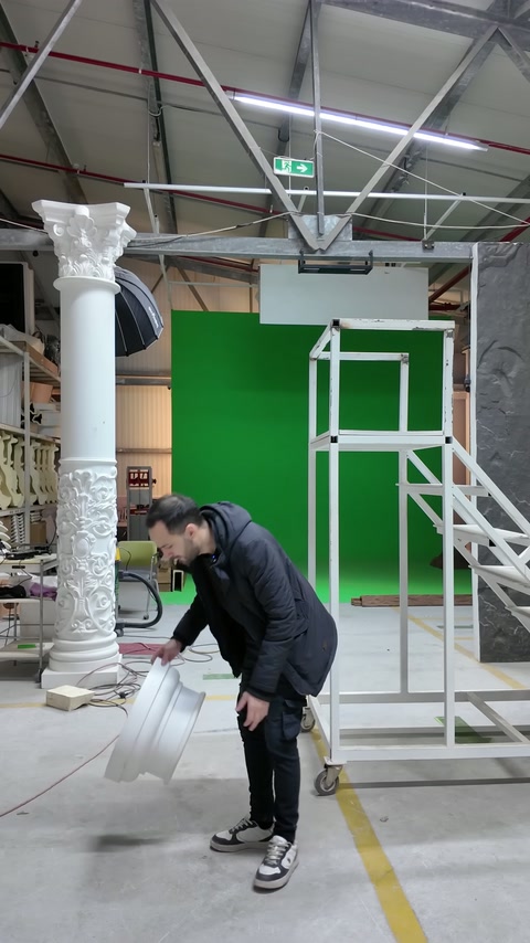 Un artigiano si china per sollevare un elemento decorativo curvo sul pavimento dell'officina.