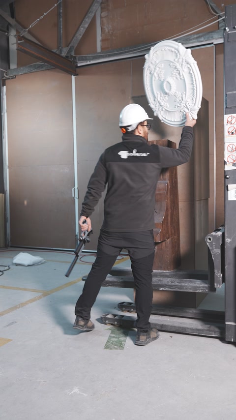 Worker holds an ornate medallion beside a wood-look beam during testing.