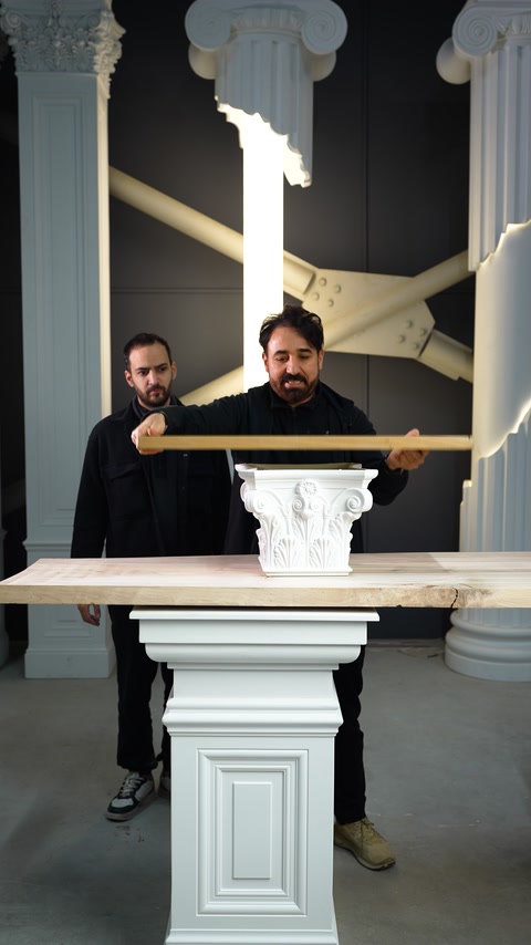 Two workers position a plank across decorative capitals for strength testing.