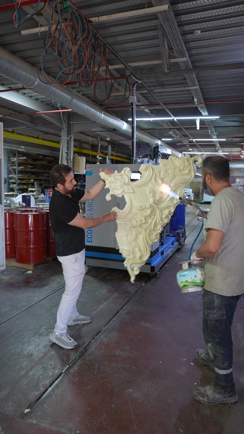 Workers handle a large ornate relief inside the production workshop.