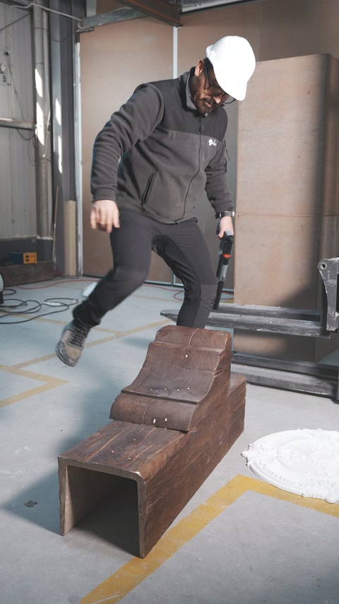 A worker steps onto a hollow wood-look beam on the workshop floor.