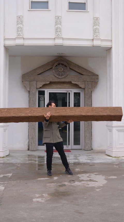 A man lifts a long wood-look beam outside the decorated building.