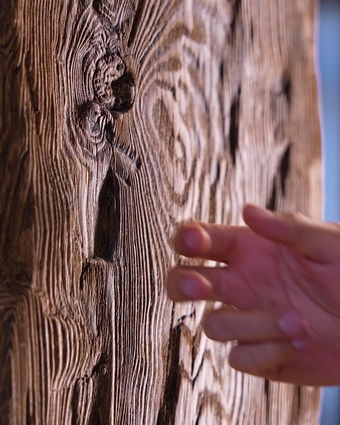 Dettaglio della texture su un pannello in poliuretano effetto legno indicato con un dito