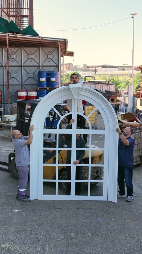 I lavoratori sostengono la finestra ad arco assemblata e la sua cornice decorativa esterna