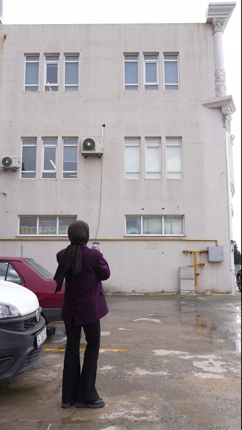 Yapıya arkası dönük sunucu üst kat pencerelerini işaret ediyor