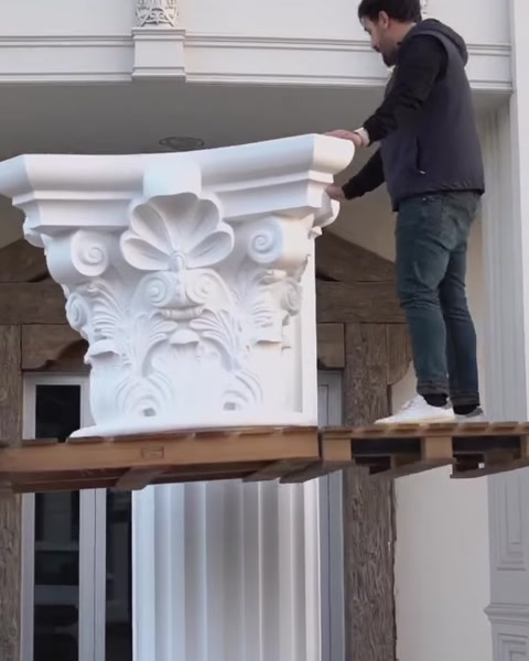 Worker lifts Corinthian capital onto elevated platform for column.