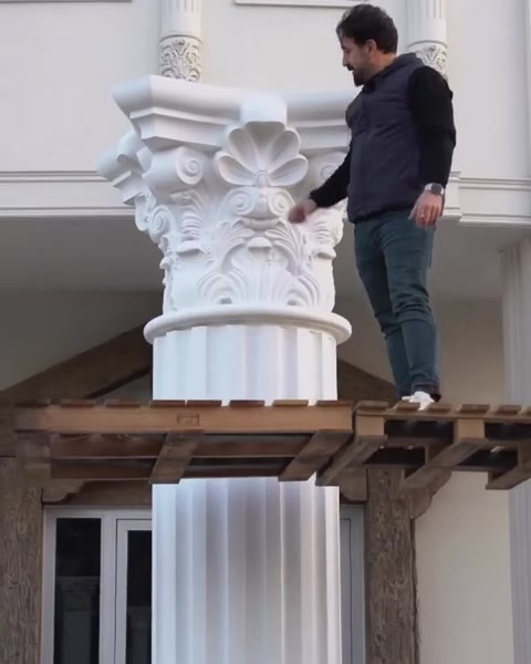 Installer fits ornate capital atop column shaft outdoors.