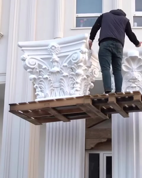 Worker stands on platform beside lifted capital near column.