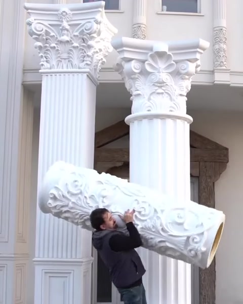 Worker lifts ornate capital piece toward column top.