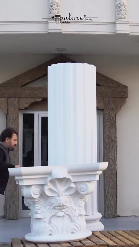 Installer positions capital piece near column top on facade.