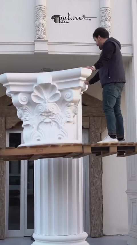 Worker lifts Corinthian capital onto elevated platform for column.