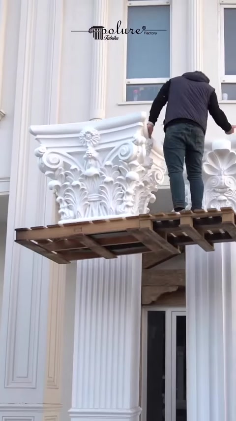 Worker stands on platform beside lifted capital near column.