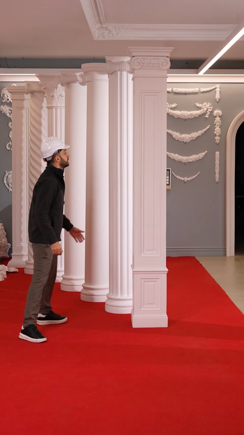 Worker stands among columns near a wall decorated with floral garlands.