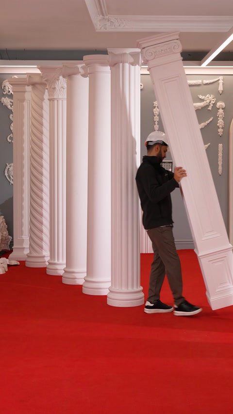 Craftsman tilts a tall fluted column beside ornamental garland wall panels.