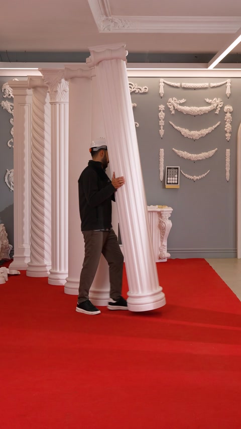 Worker carries a tilted fluted column through the fireplace display room.