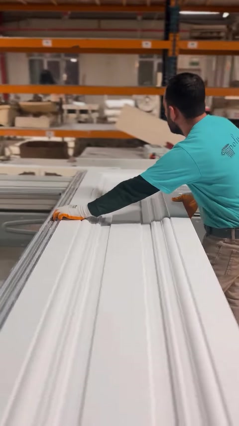 Un operatore guida un profilo decorativo per contorni di finestre sul banco di lavoro