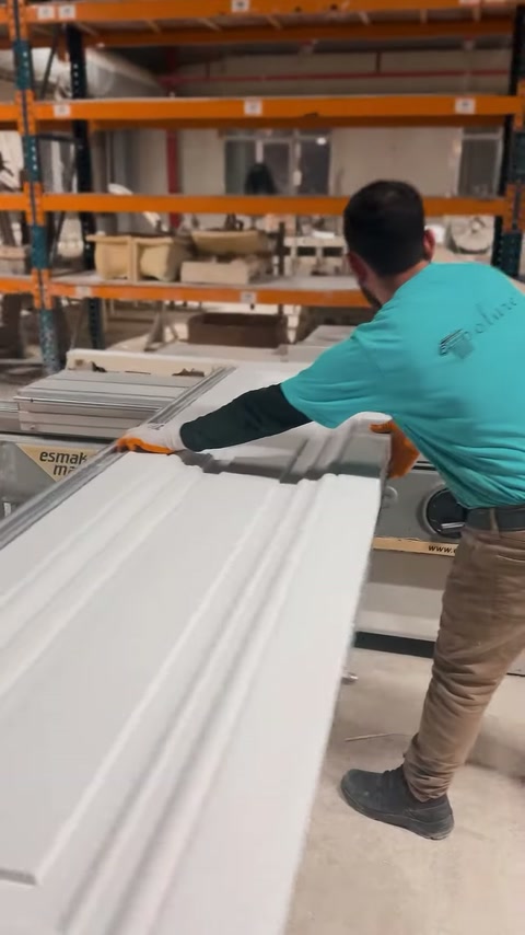 Artigiano che posiziona manualmente una larga cornice in poliuretano sul banco di lavoro dell'officina