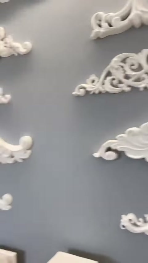 Sulla parete grigia della showroom sono presenti piccoli elementi decorativi bianchi ricurvi.