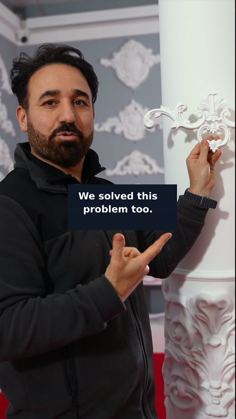 Il presentatore mostra una decorazione con motivi a volute accanto a una colonna circolare della showroom.