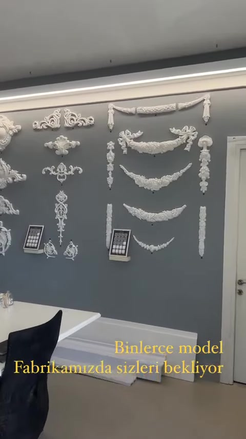 Decorazioni classiche bianche di diverse dimensioni sono disposte su una parete espositiva grigia