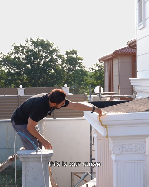 A craftsman bends over at the roof edge to install a moulding