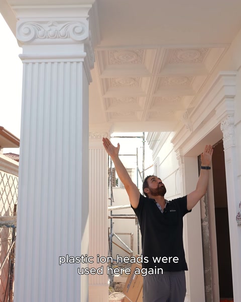 A craftsman reaches by hand toward a ceiling detail between column capitals