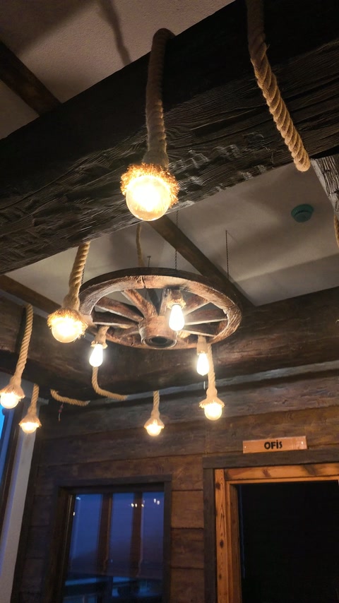 Wagon-wheel pendant hangs among rustic beams and rope-mounted bulbs.