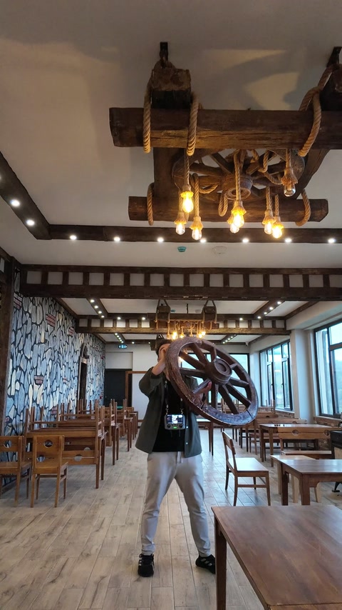 Spacious dining hall combines decorative ceiling beams with wheel lighting.