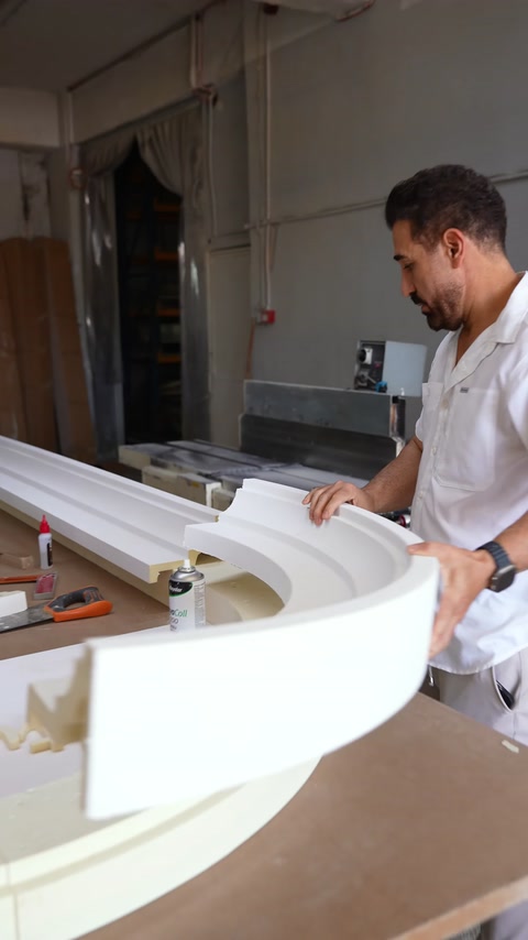 Un operaio leviga una modanatura ad arco curva in poliuretano sulla linea di produzione